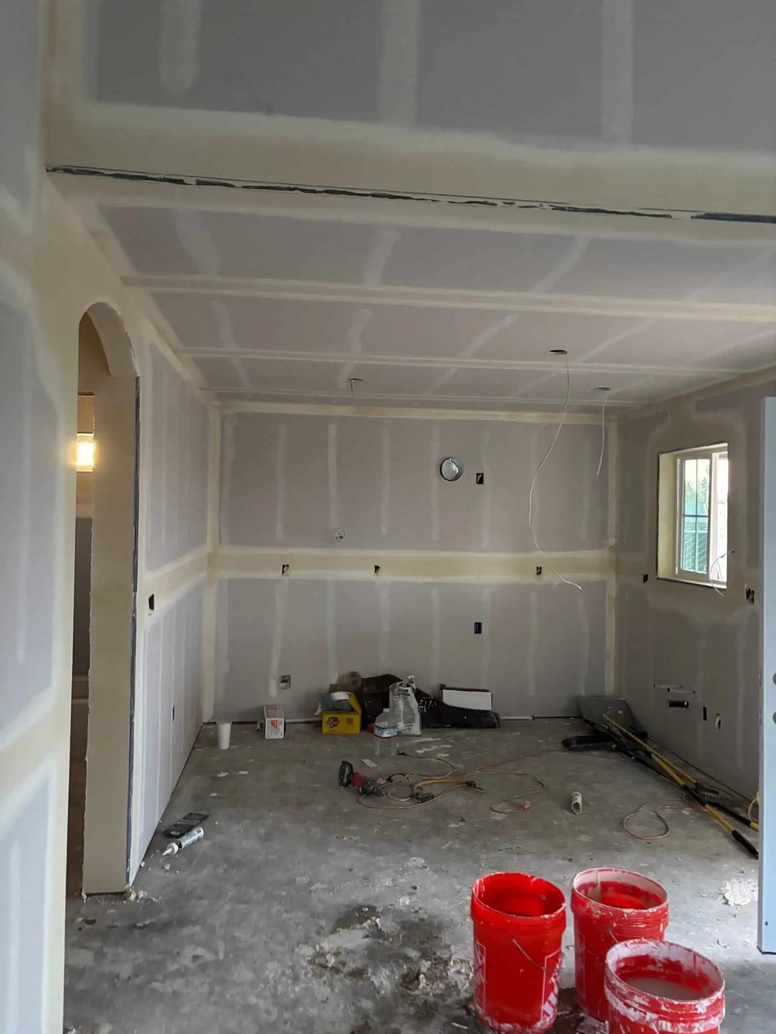 Newly installed drywall in a room under construction with tools and materials present.