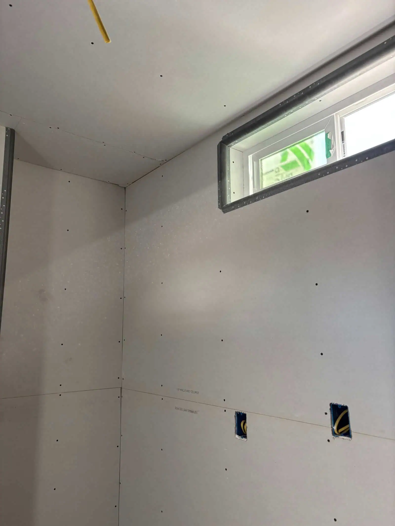 Interior drywall installation with window opening in a construction site.