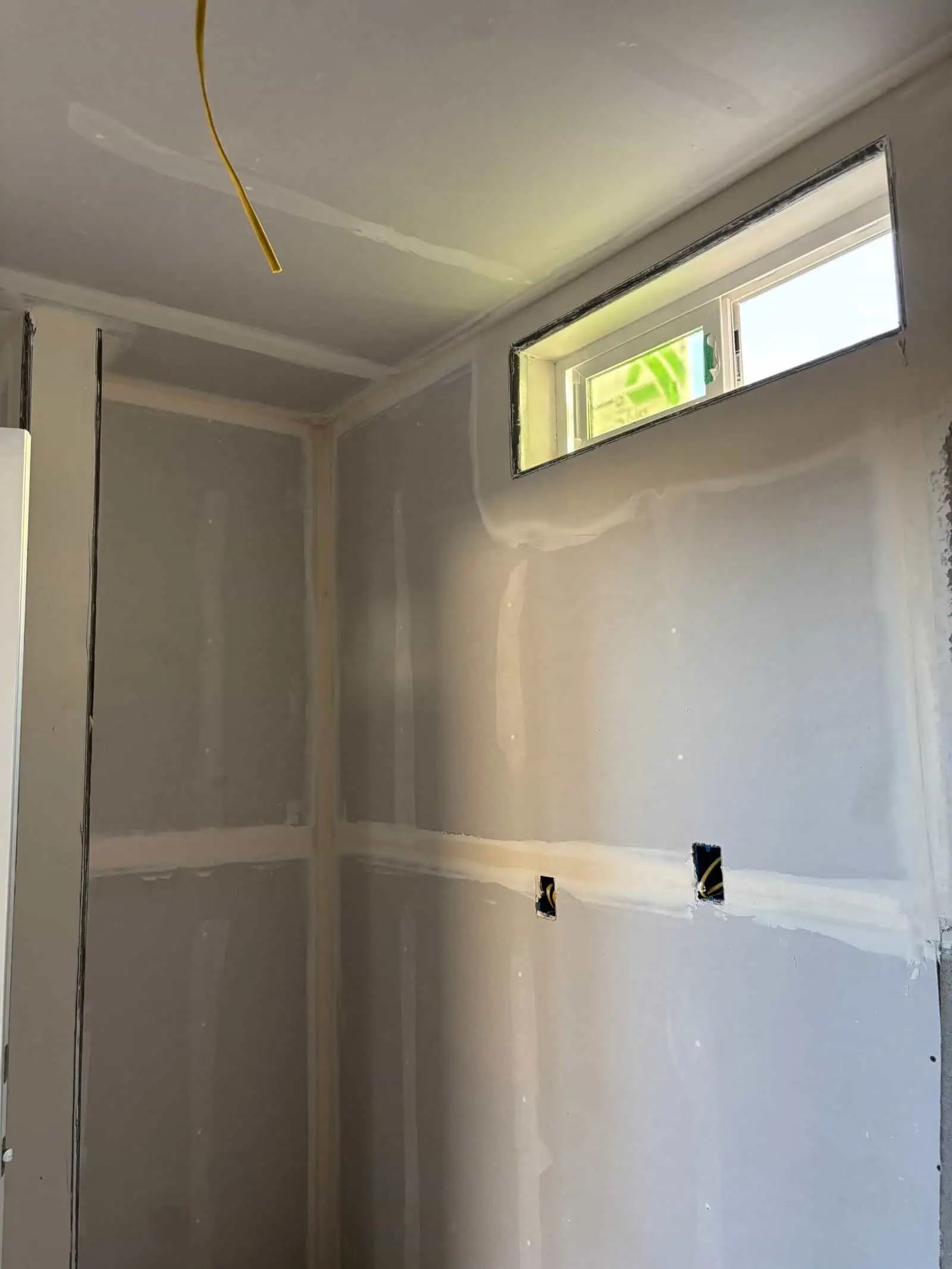 Interior drywall installation with window in a construction site.