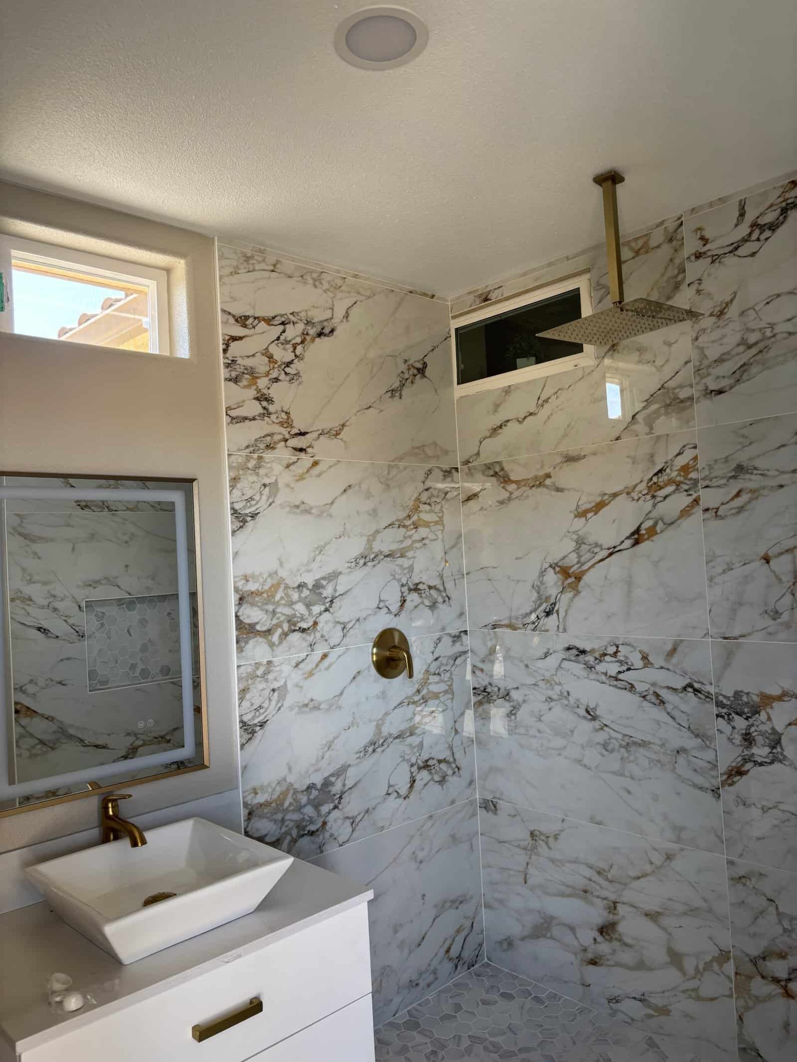Modern marble shower with gold fixtures and window in bathroom.